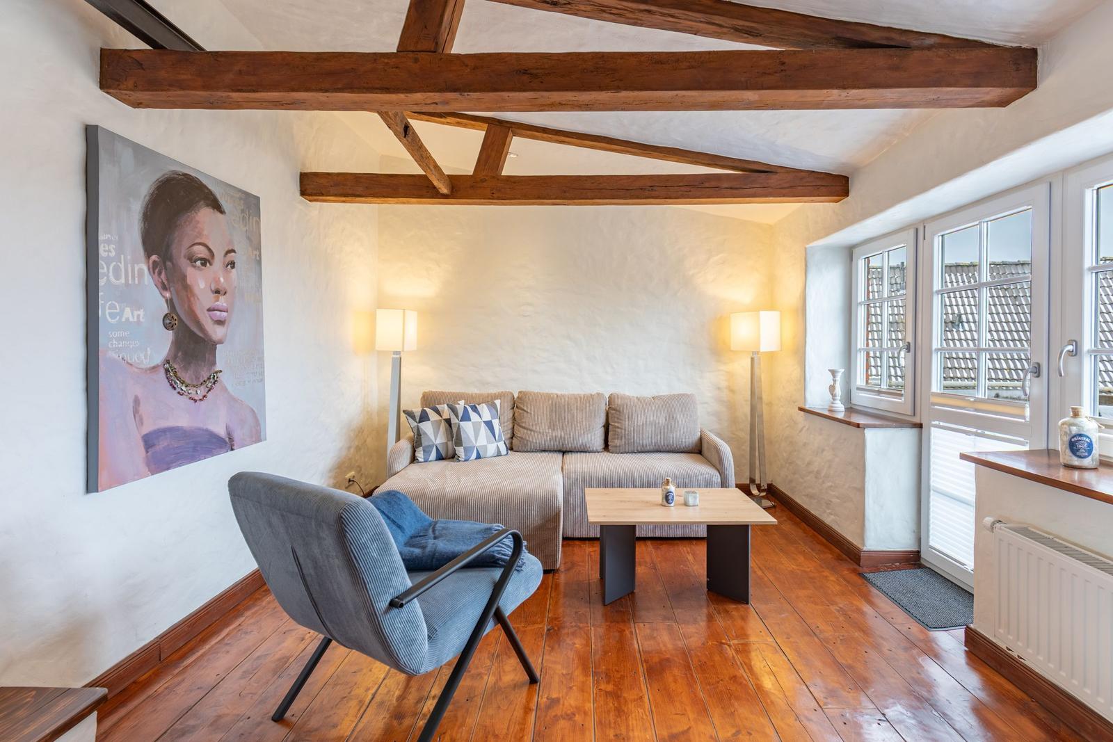 Living room with wooden beams, sofa, armchair, and large window.