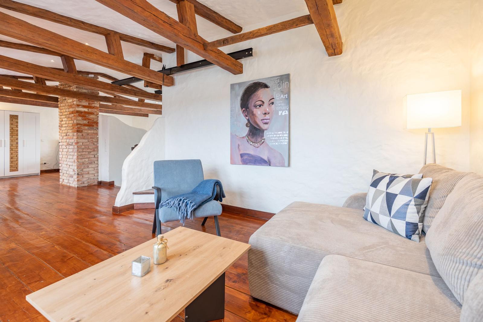 Living room with sofa, chair, table, and wooden beam ceiling.