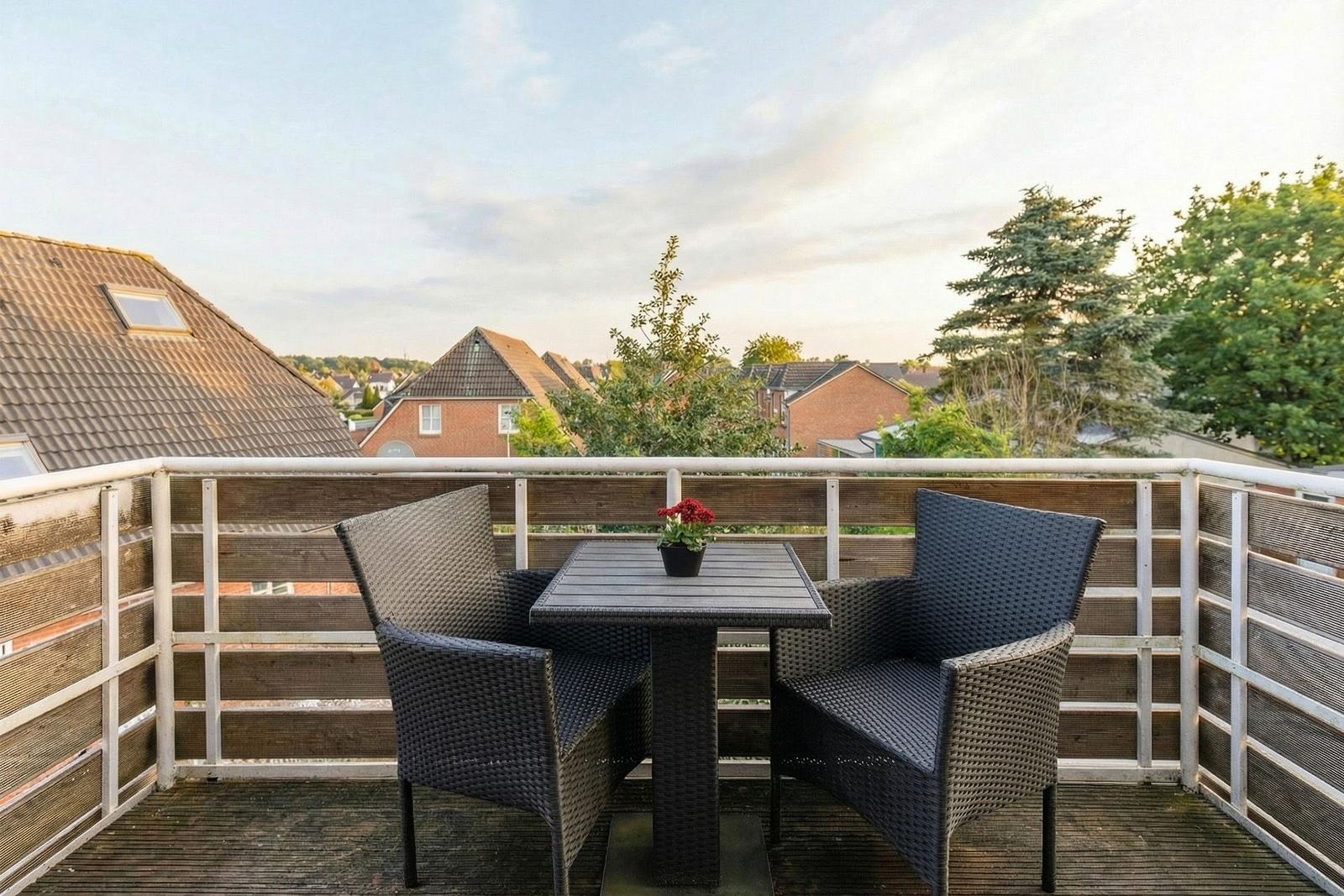 Terrace with table and two chairs, view of rooftops and trees.