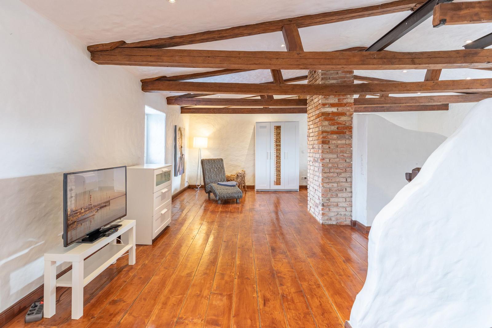 Room with wooden beams, hardwood floor, and TV on white stand.