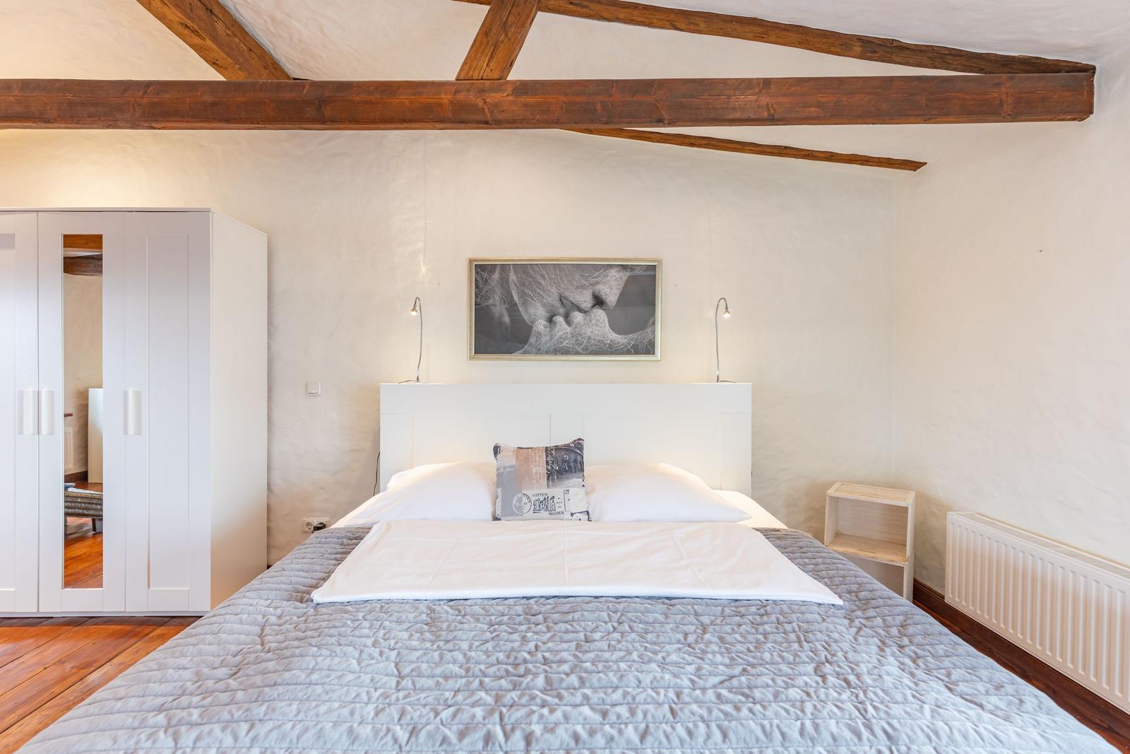 Bedroom with bed, wardrobe, and wooden beams on the ceiling.