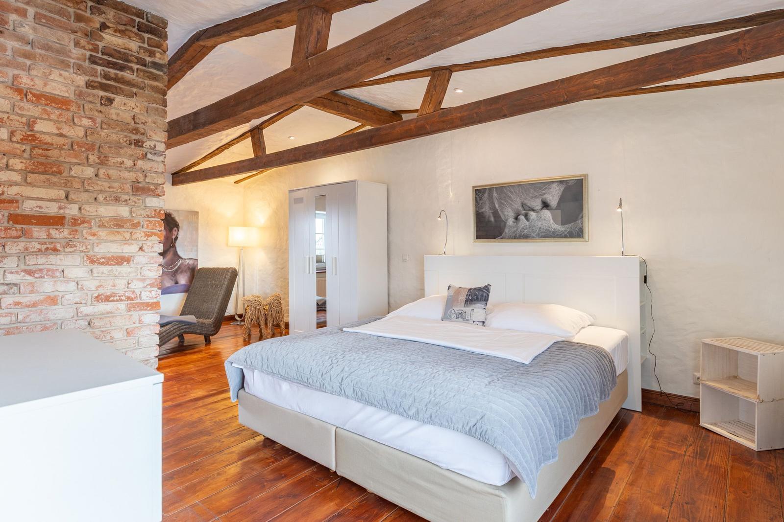 Bedroom with wooden beam ceiling, bed, wardrobe, and hardwood floor.