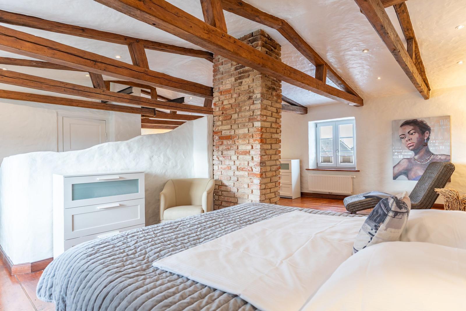 Bedroom with wooden beam ceiling, brick pillar, and bed with gray quilt.