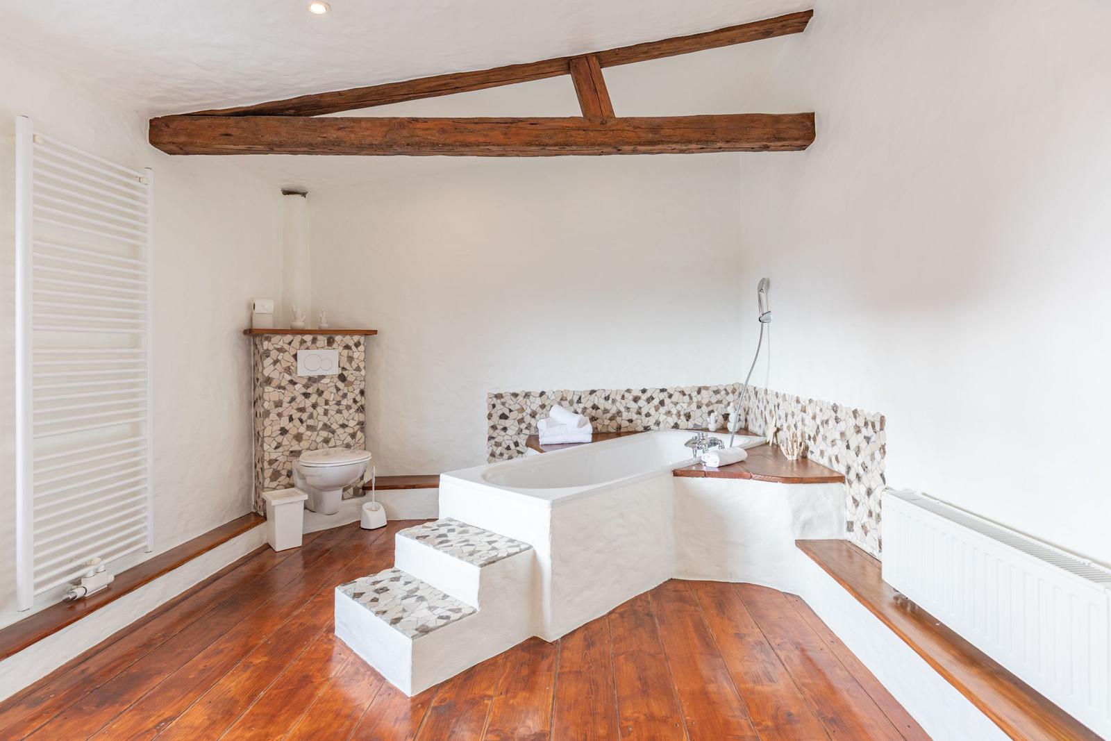 Bathroom with bathtub, toilet, and wooden beams on the ceiling.