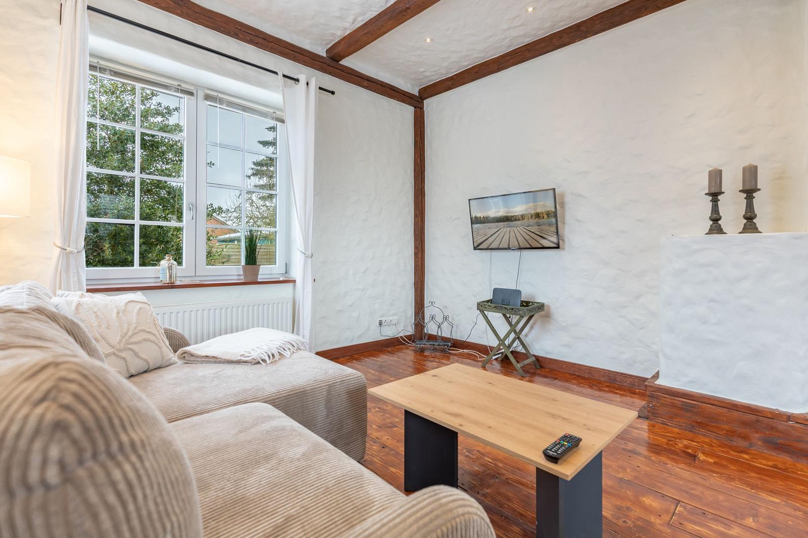Living room with sofa, TV, and wooden floor. Window with view of garden.