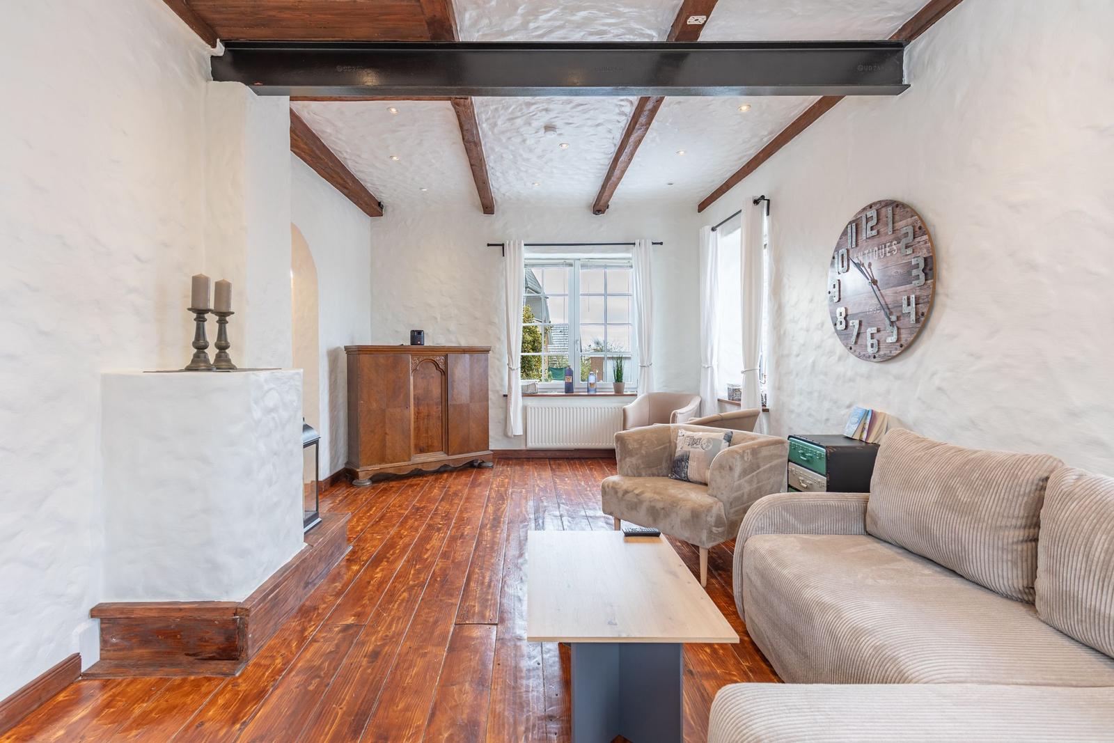 Living room with wooden floor, fireplace, sofa, and wall clock.