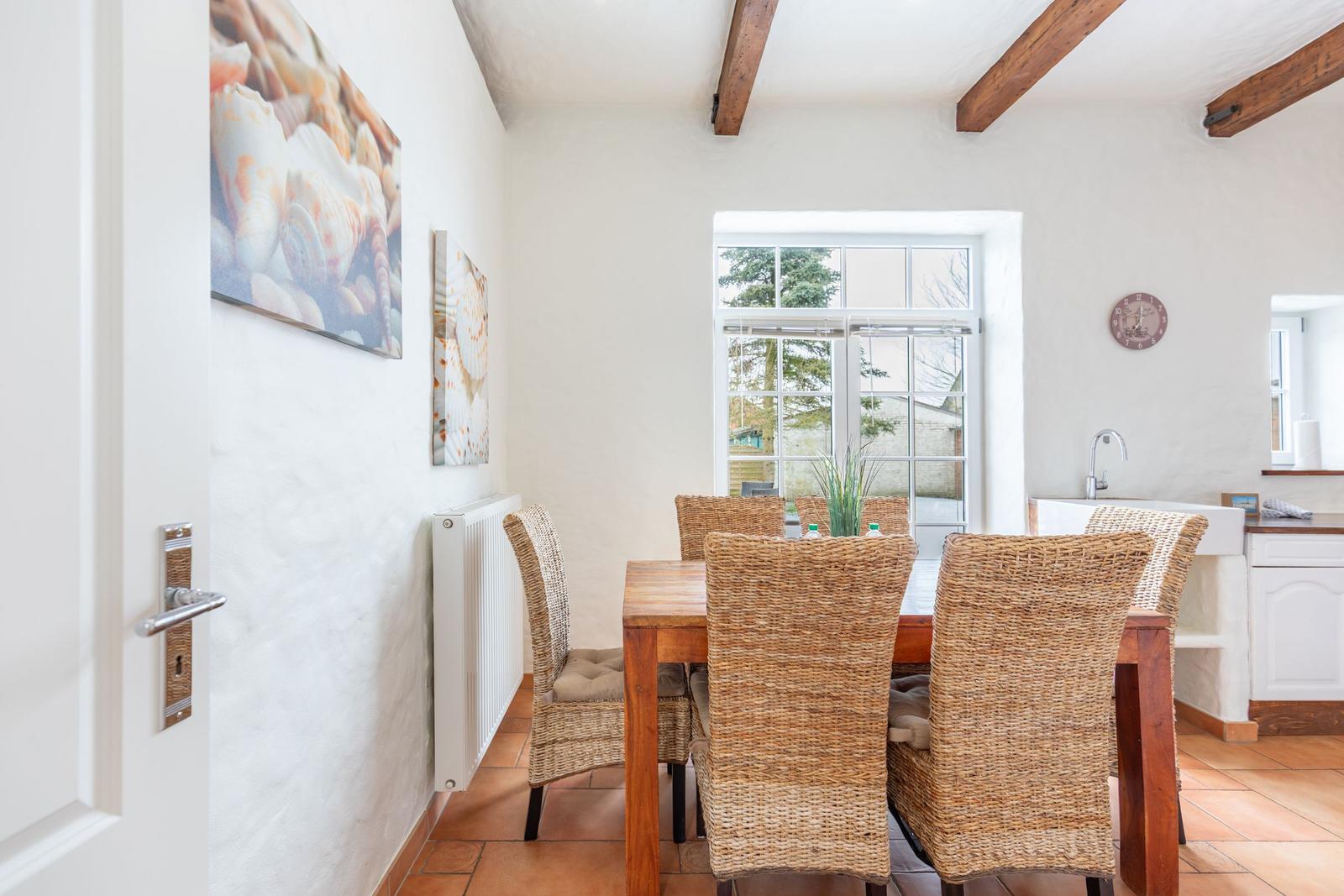 Dining room with wooden table, wicker chairs, and window to the garden.