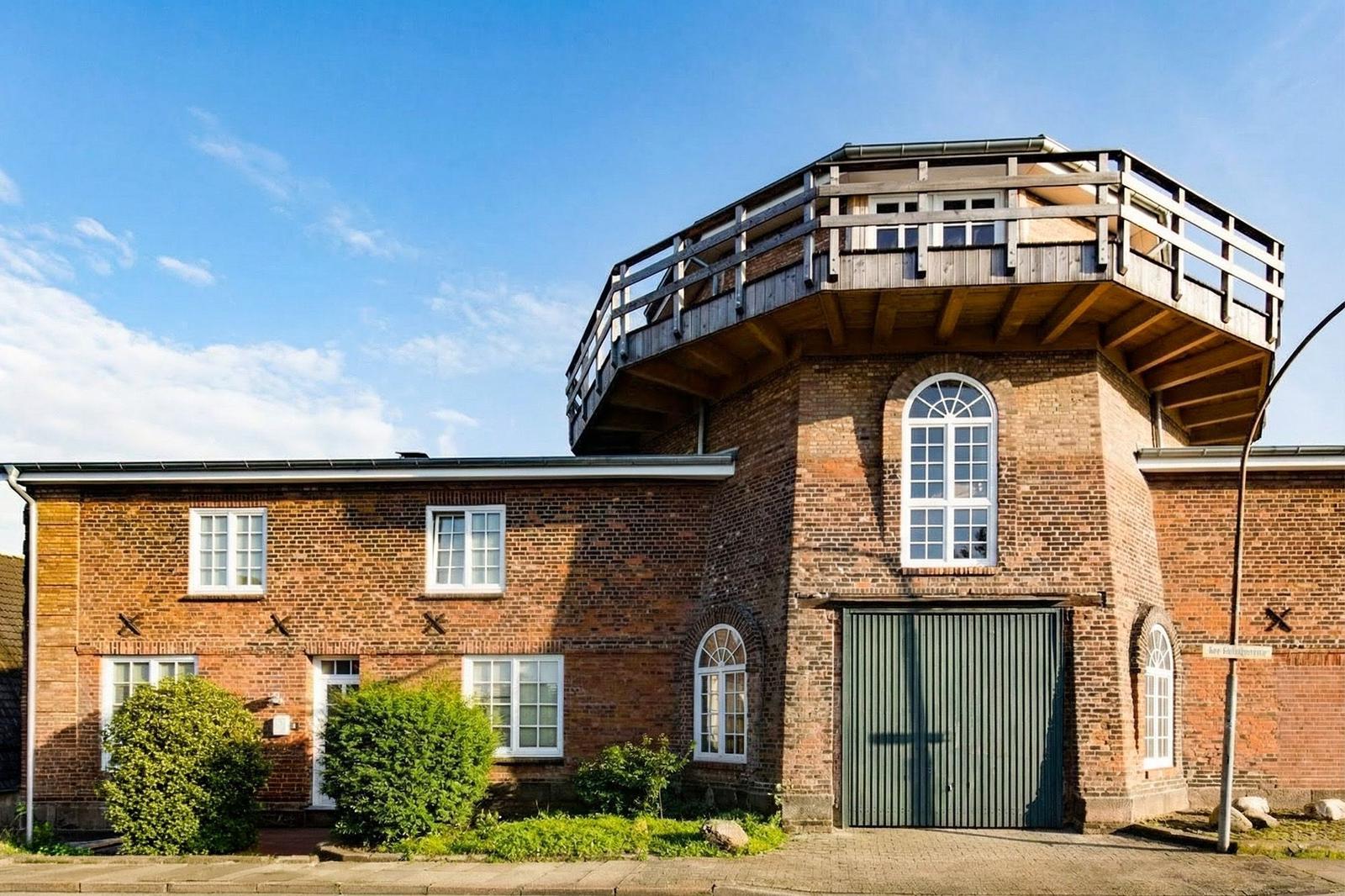 Two-story brick house with wooden terrace and green garage door.