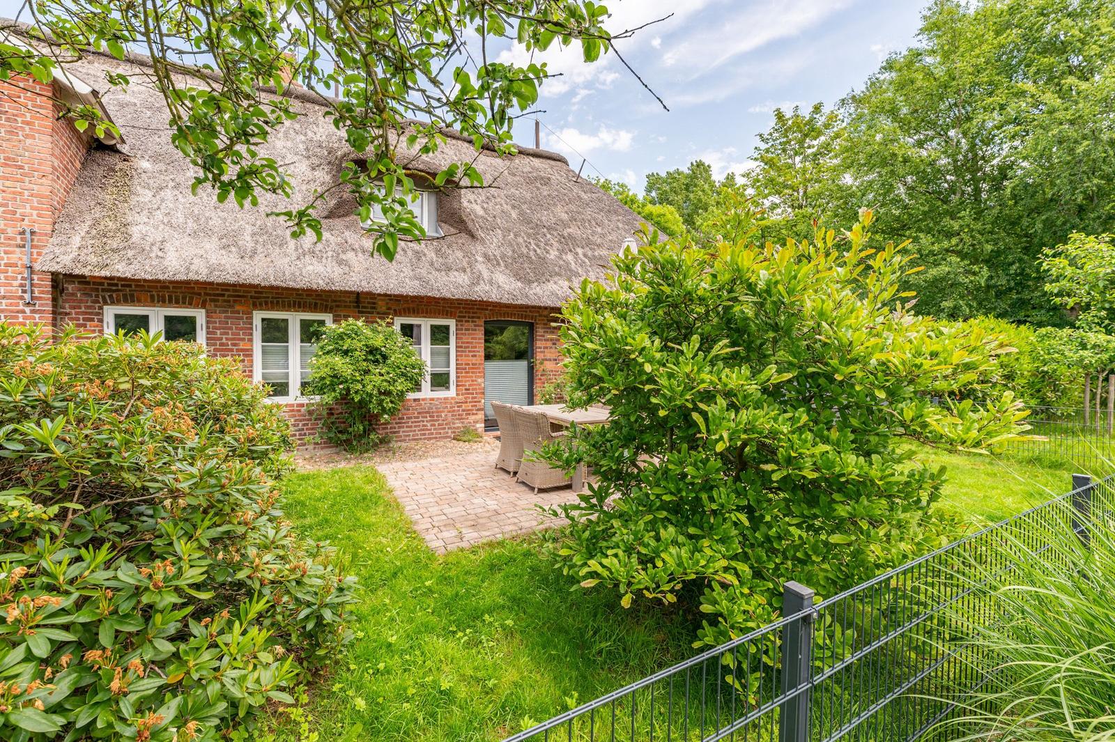 House with thatched roof, garden, and terrace with seating area.