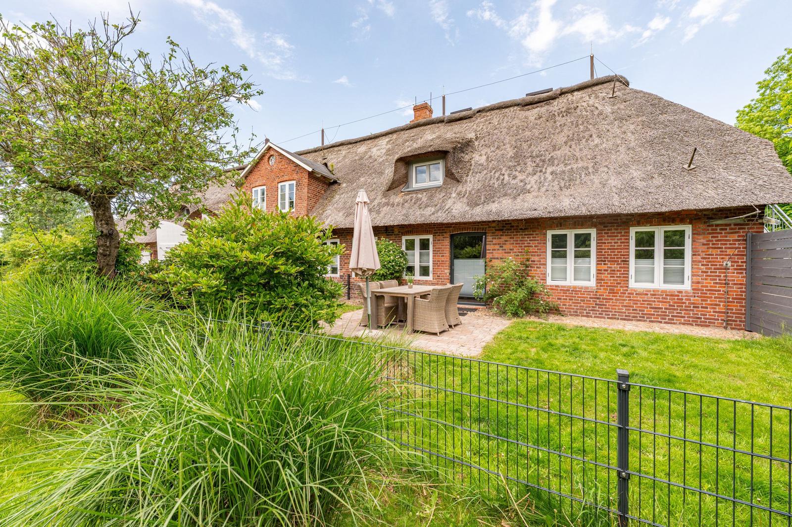 Red brick house with thatched roof and garden area with table and chairs.