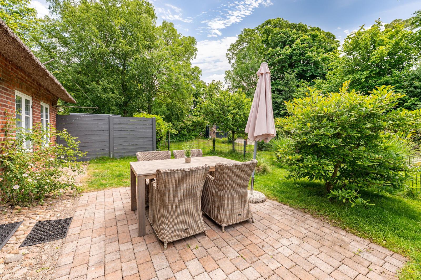 Terrace with table and chairs, surrounded by greenery and a closed parasol.