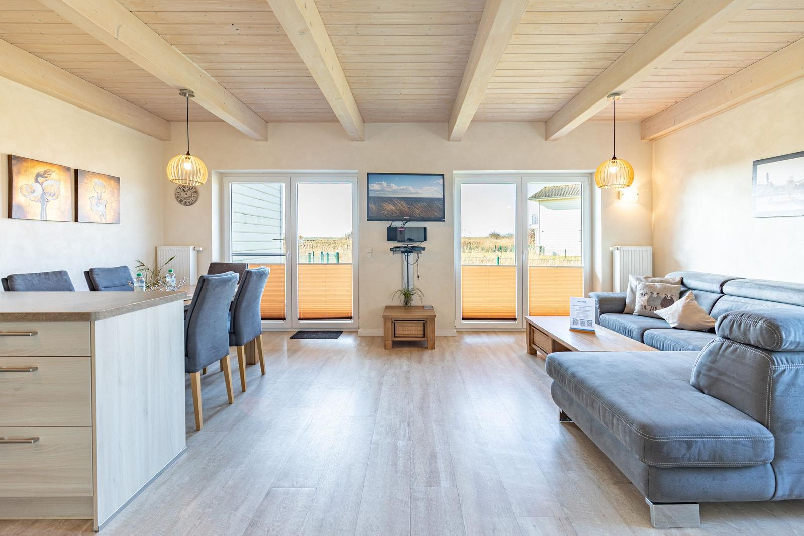 Living and dining area with sofa, dining table, and TV. Wooden ceiling and large windows.