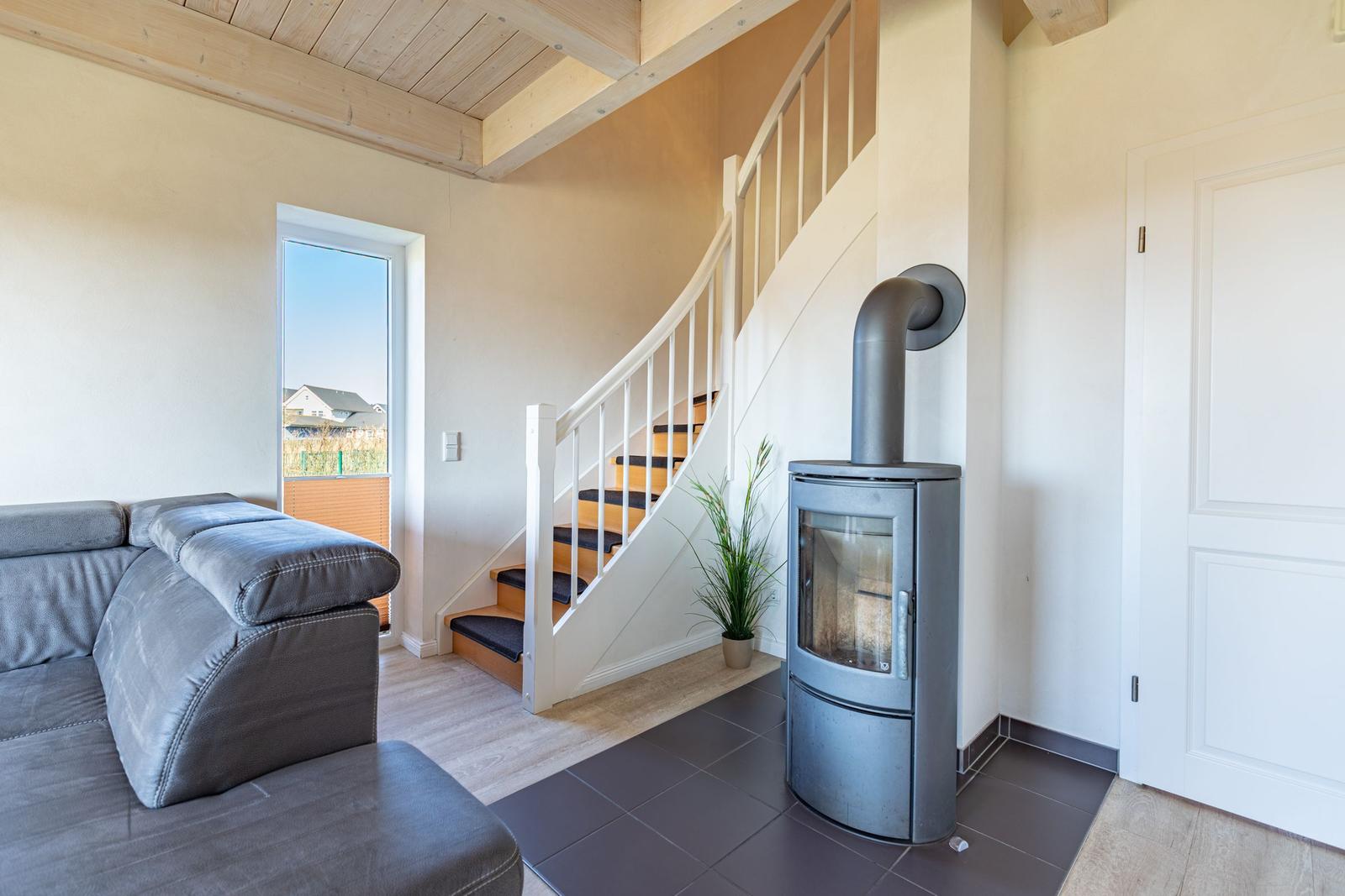Living area with sofa, staircase, and wood stove. Window shows outdoor area.