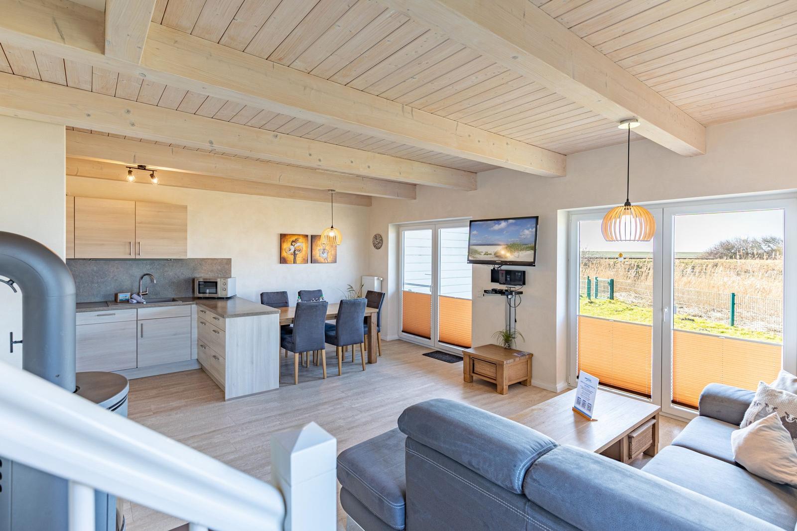 Living and dining area with kitchen, sofa, and TV. Wooden ceiling and large windows.