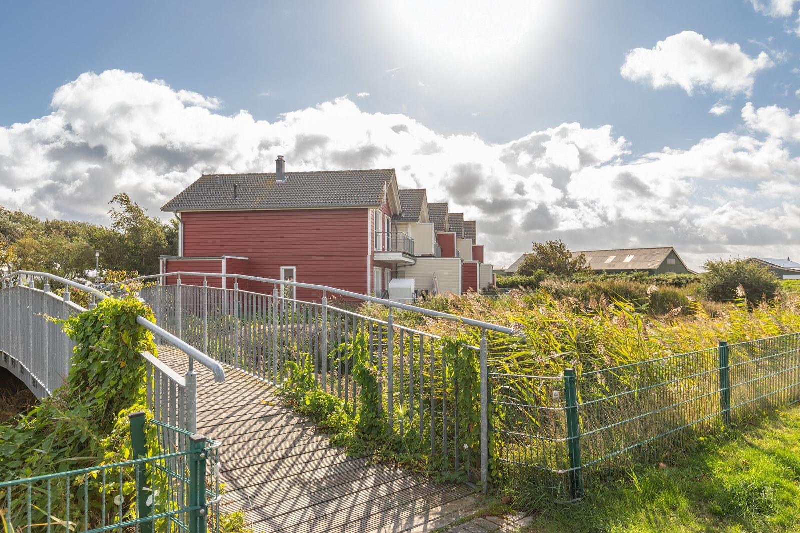 Red holiday houses with balcony, access via wooden walkway with metal railing.