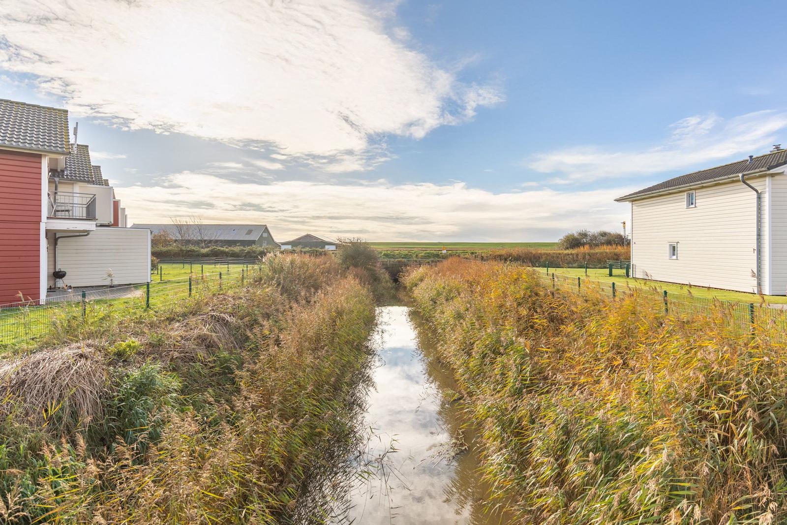 A canal flows between two houses through a green landscape.
