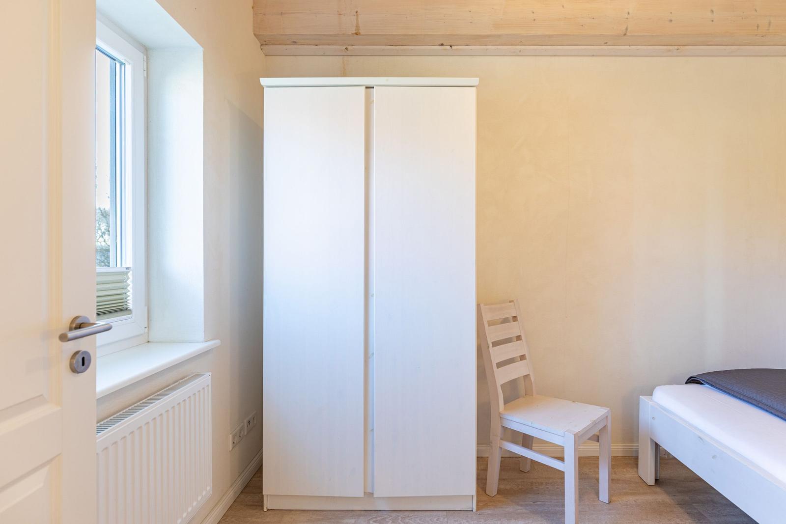 Bedroom with white wardrobe, chair, and bed. Window and radiator are visible.