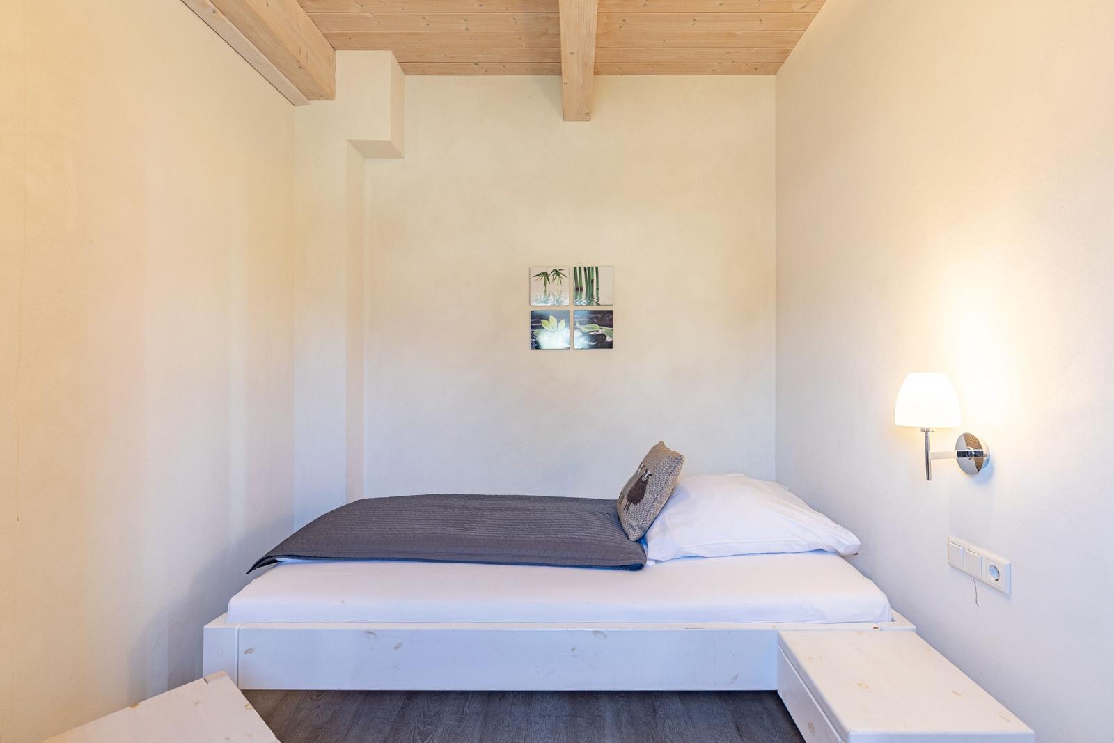 Bedroom with bed, wall lamp, and ceiling beams.