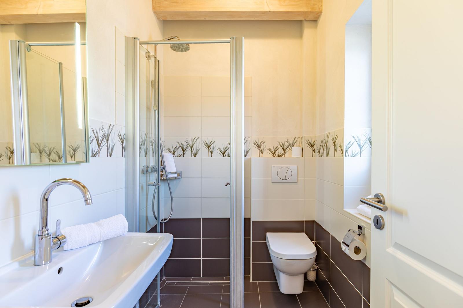 Bathroom with shower, toilet, and sink. Wall tiles with plant motif.