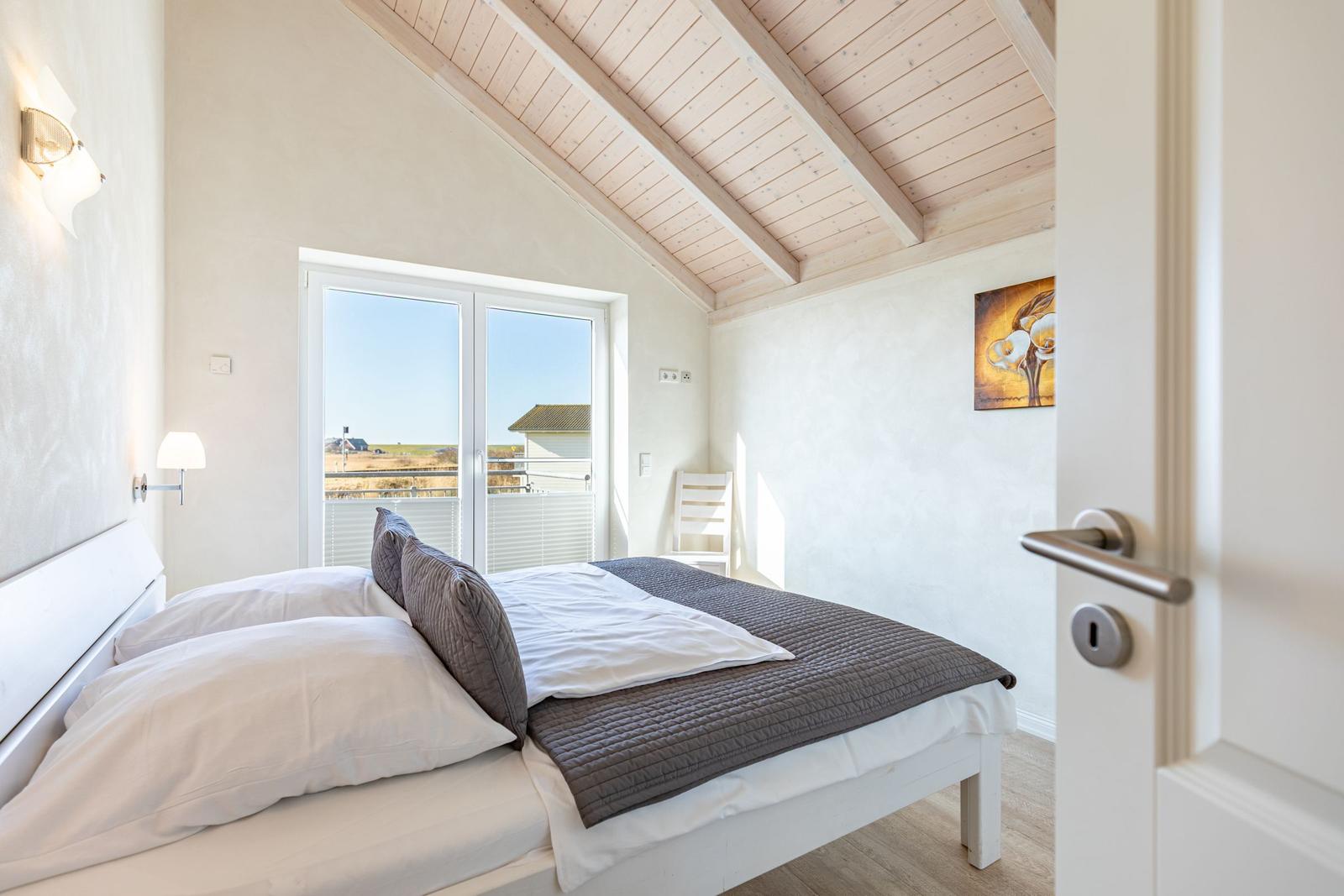 Bedroom with double bed, balcony, and wooden ceiling.