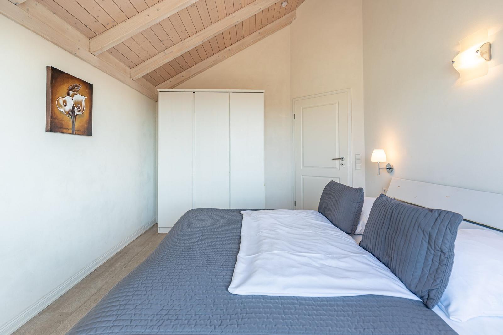 Bedroom with bed, wardrobe, and duvet. Wooden ceiling and wall art visible.