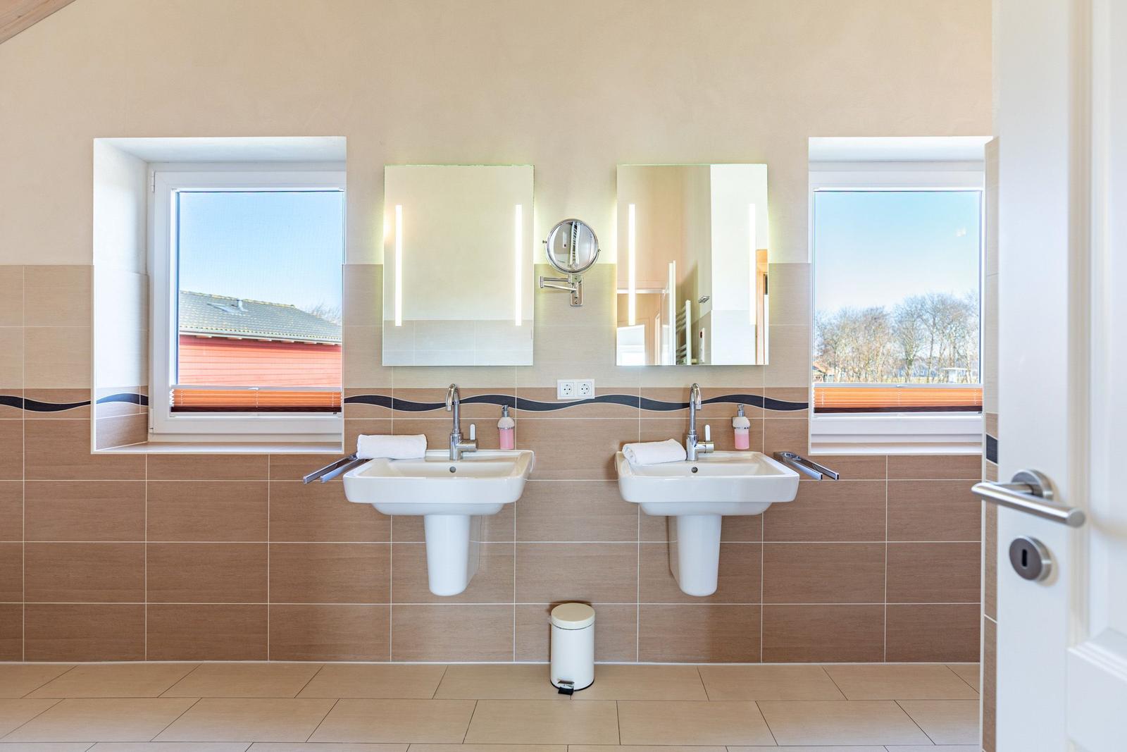 Two sinks with mirrors and windows. Tiled wall and floor.