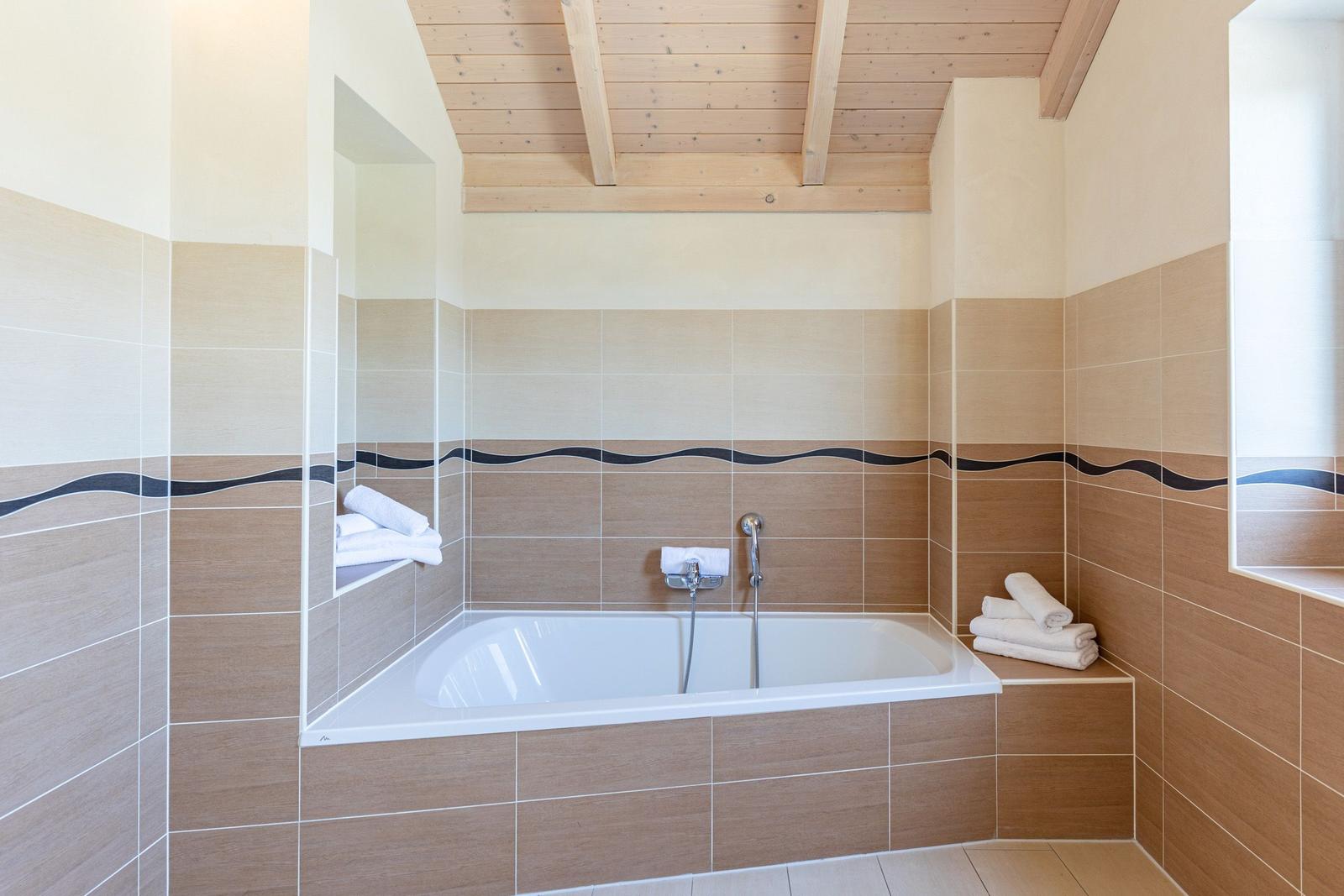 Bathroom with bathtub, wooden ceiling, and tiled walls with black wavy line.