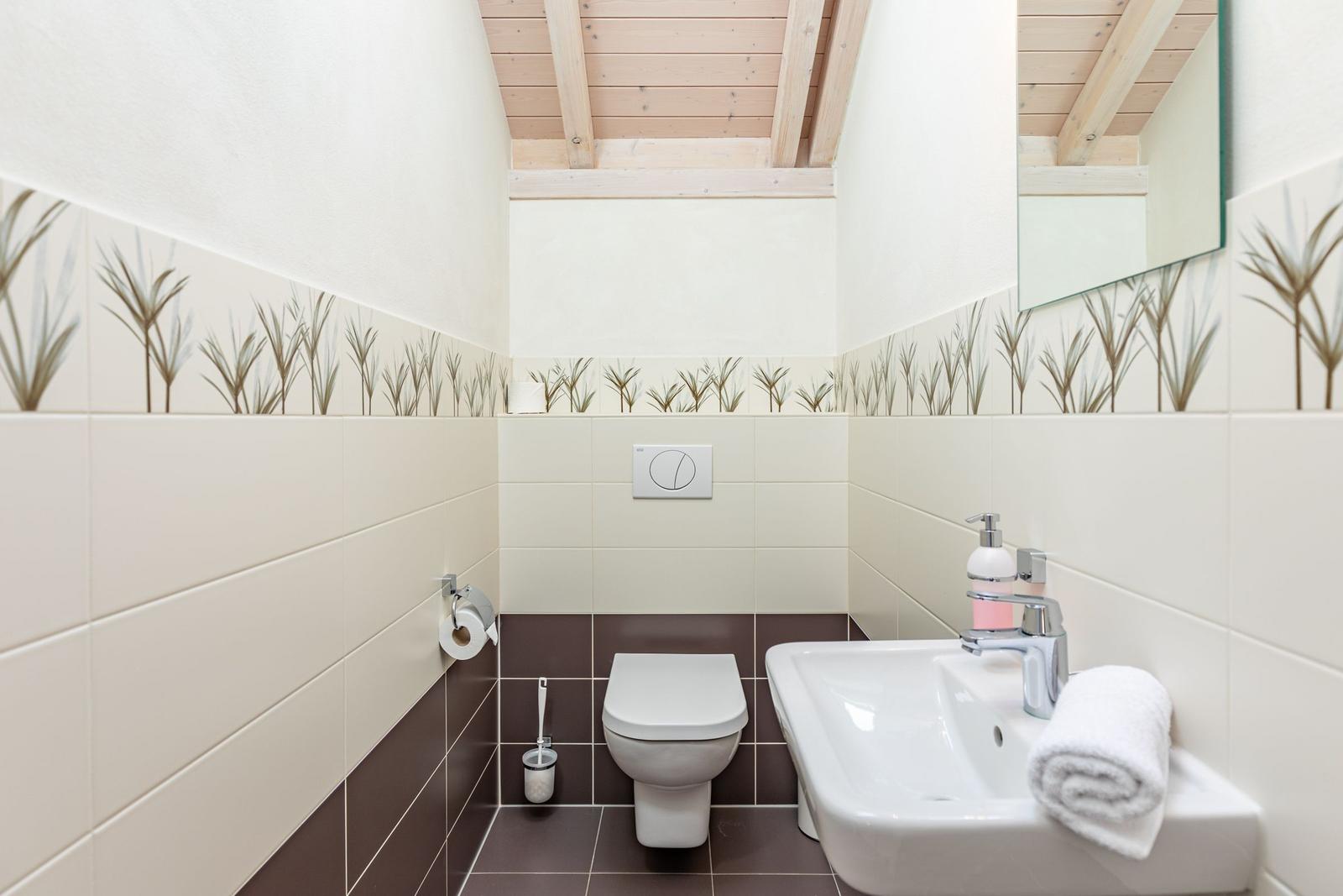 Bathroom with toilet, sink, and mirror. Wall tiles with plant motif and wooden ceiling.