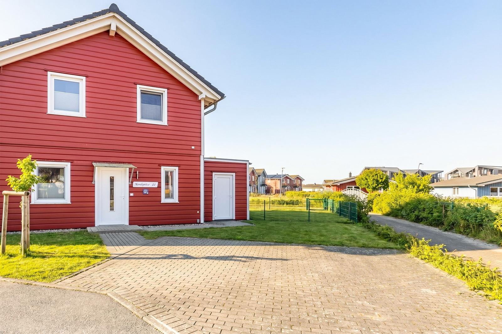 Red house with white windows and door. Front garden and paved path.
