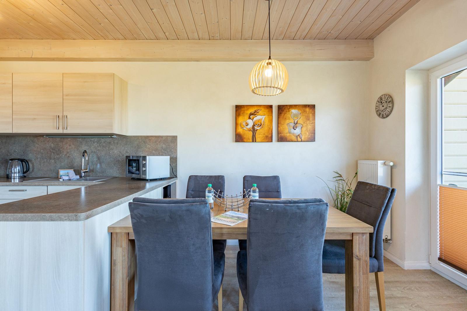 Dining area with table and chairs, kitchenette and wall art.