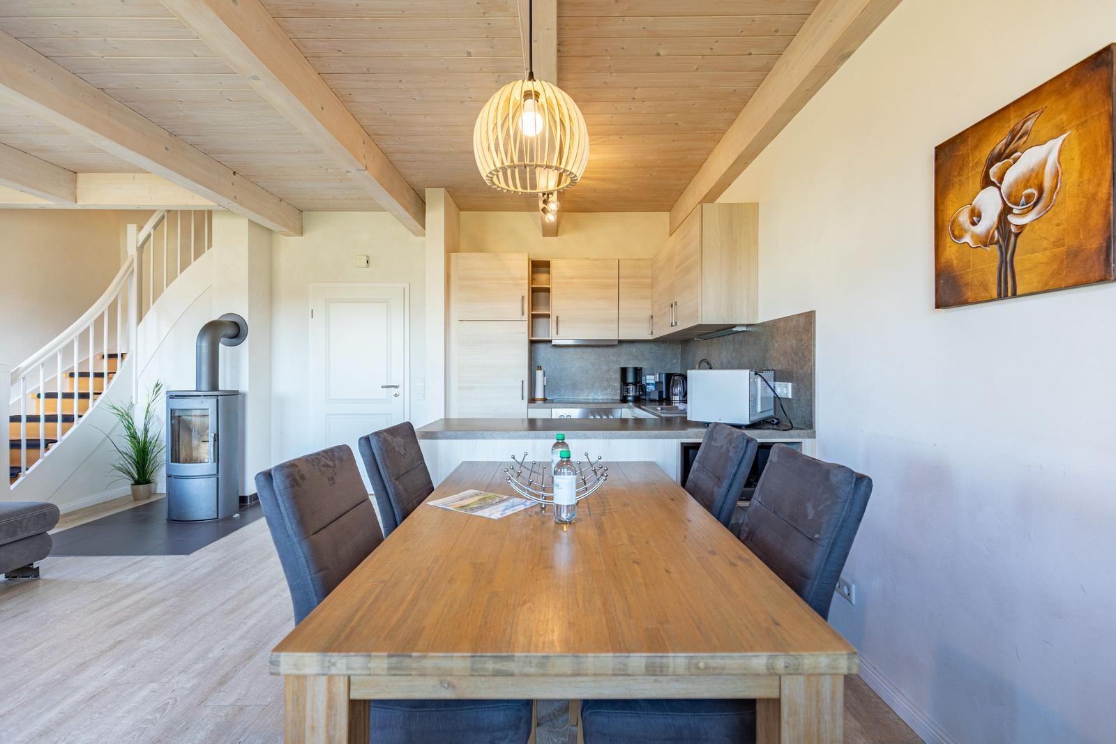 Dining area with wooden table, kitchenette, and wooden ceiling with beams.