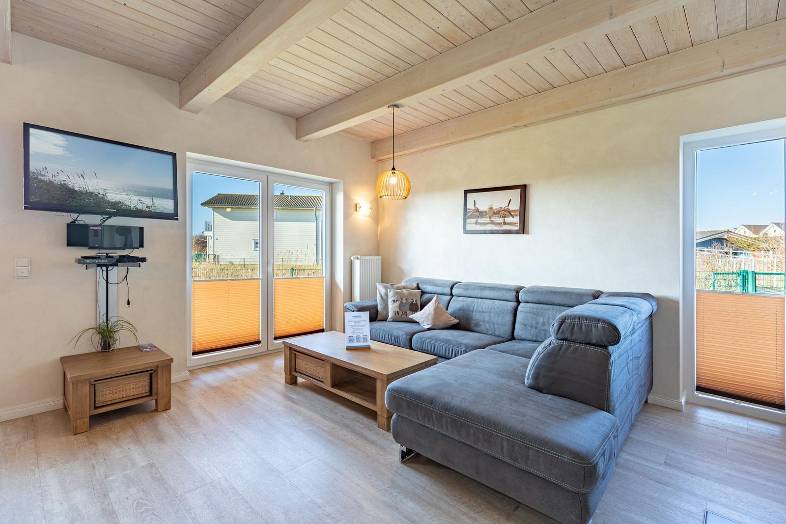 Living room with sofa, TV, and wooden floor. Large windows and balcony doors.