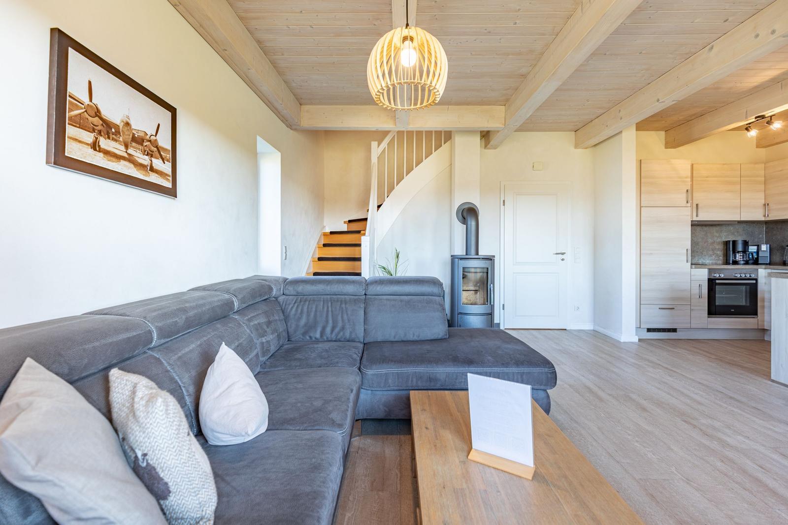 Large living area with gray sofa, wooden floor, and open kitchen in the background.