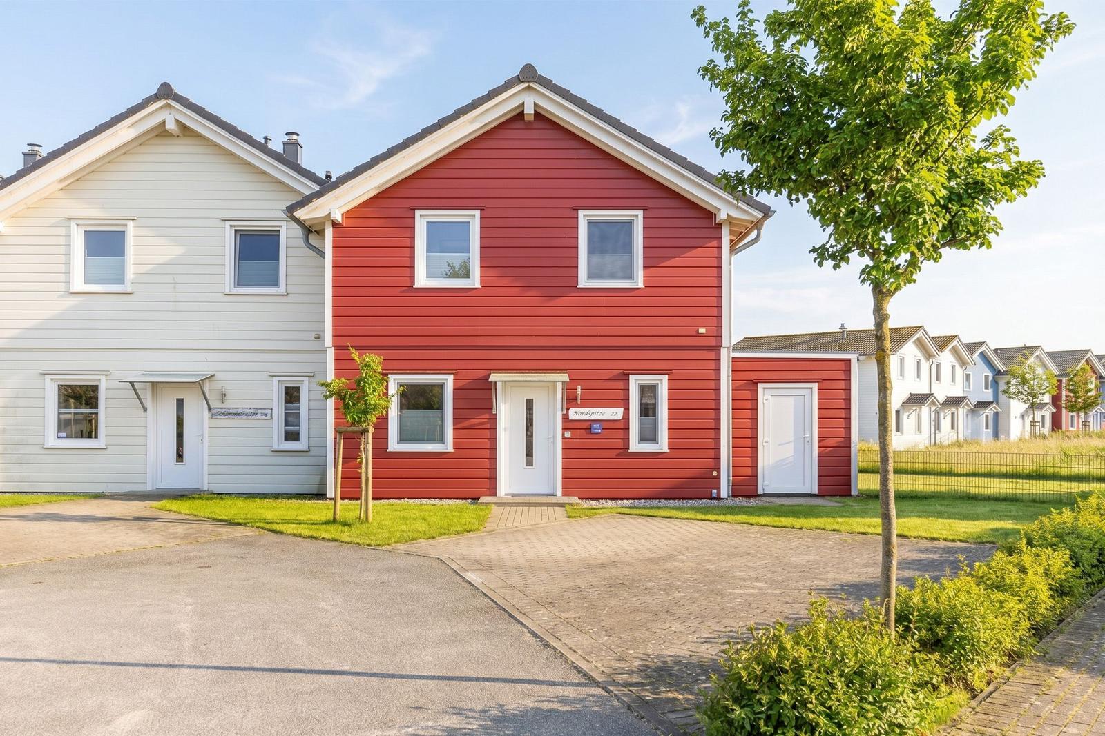 Red single-family house with white windows and front door. Green lawn and tree in front.