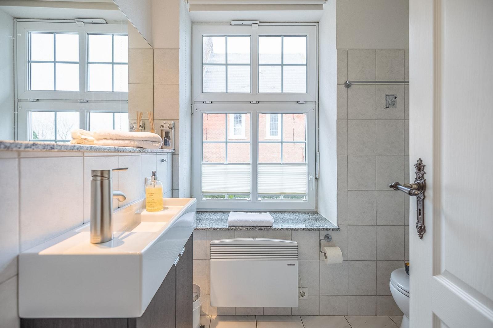 Badezimmer mit Waschbecken, Toilette und Fenster mit Blick auf Gebäude.