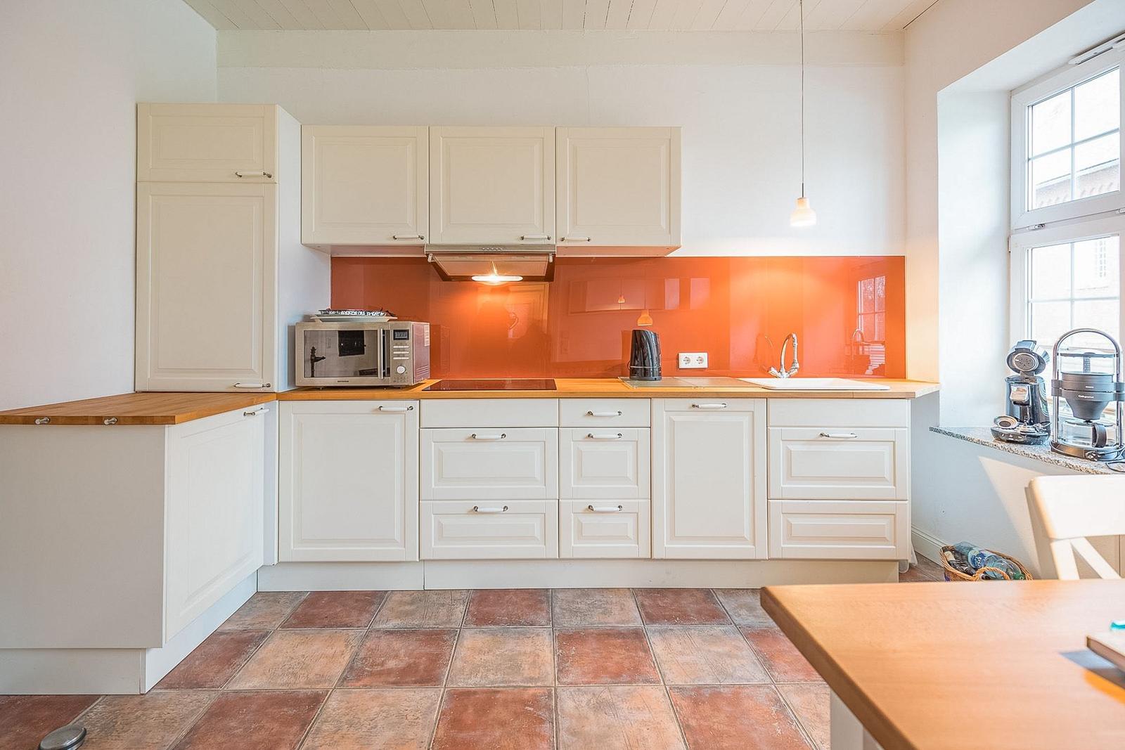Küche mit weißen Schränken, orangefarbener Rückwand und Holzoberflächen.