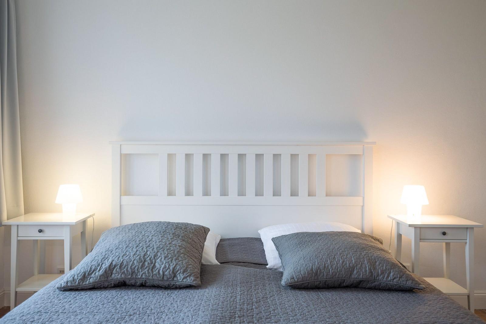 Ein Bett mit grauer Bettwäsche und zwei Nachttischen mit Lampen.