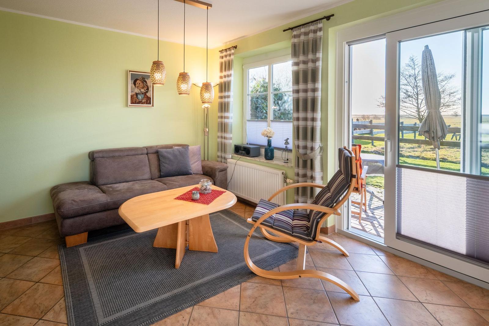 Wohnzimmer mit Sofa, Tisch und Sessel. Durchgang zur Terrasse mit Blick auf Feld.