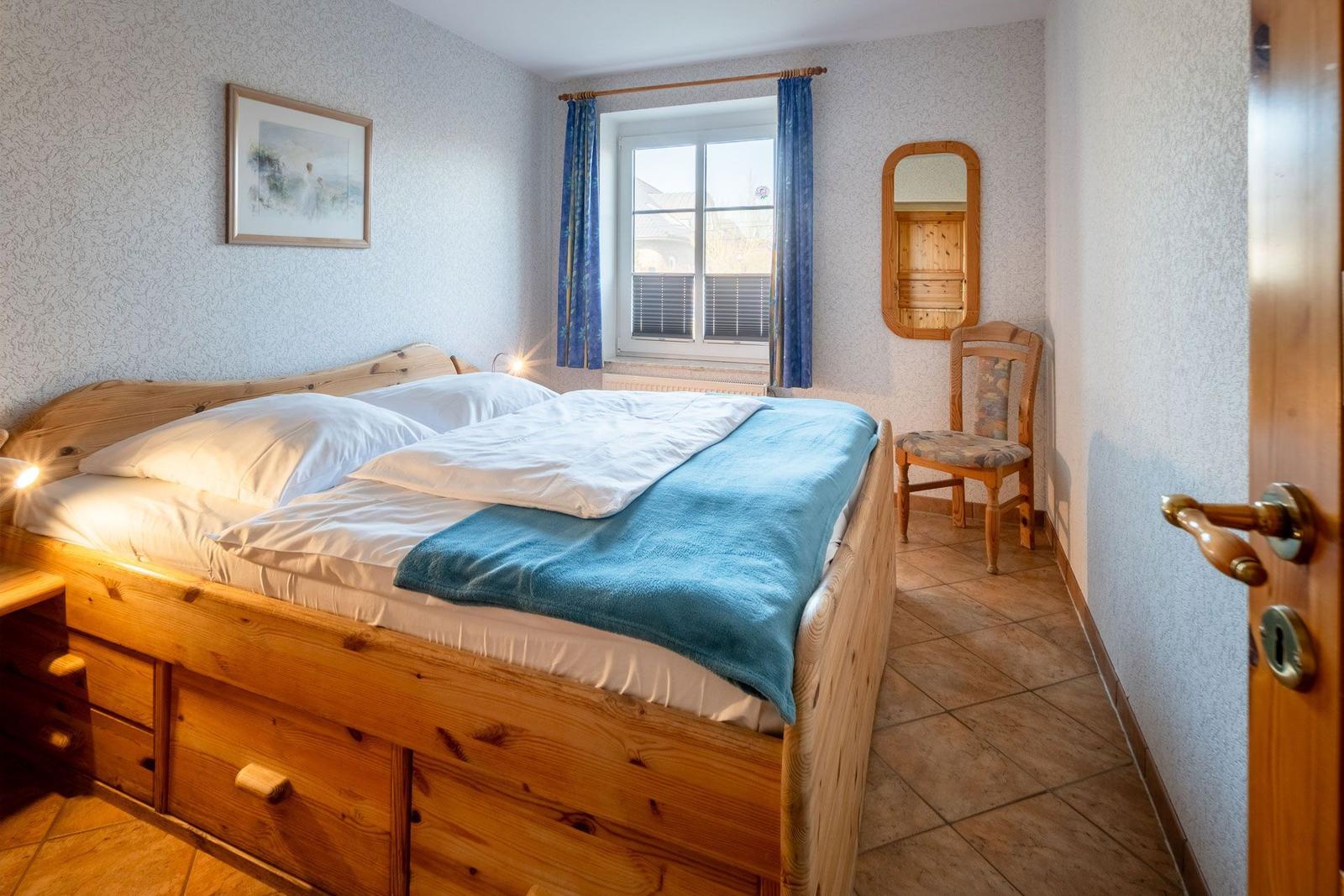 Ein Schlafzimmer mit Holzbett, blauen Vorhängen und Stuhl neben dem Fenster.