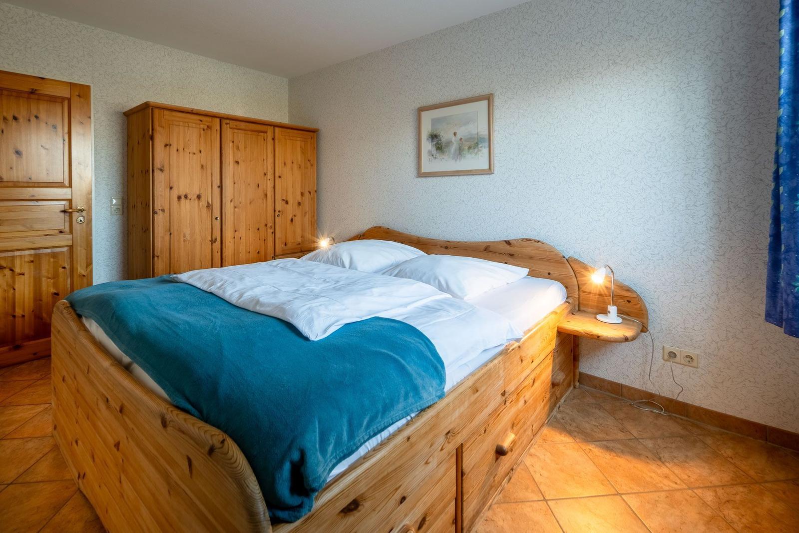 Schlafzimmer mit Holzbett, Kleiderschrank und Nachttischlampe.