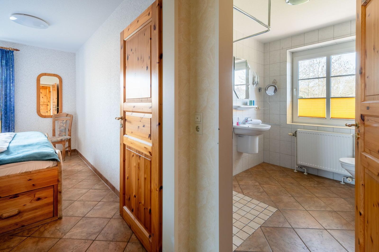 Schlafzimmer mit Bett und Spiegel. Nebenraum ist Bad mit Waschbecken und Toilette.