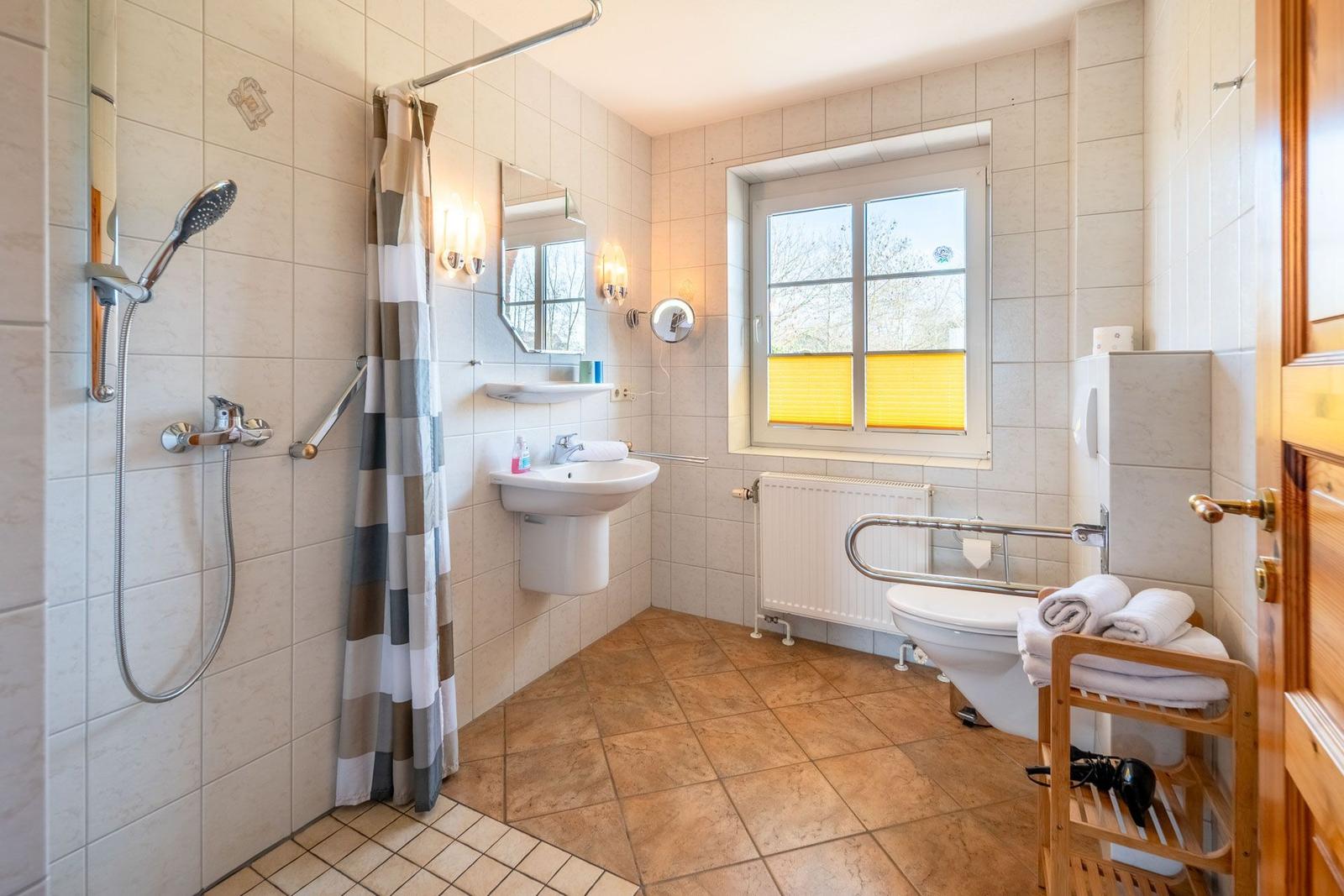 Badezimmer mit Dusche, Waschbecken und WC. Fenster mit gelben Jalousien.