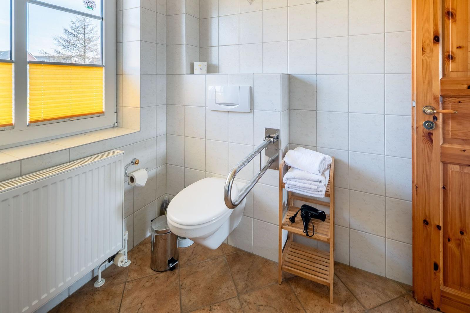Badezimmer mit WC, Handtuchständer und Fenster mit Jalousie.