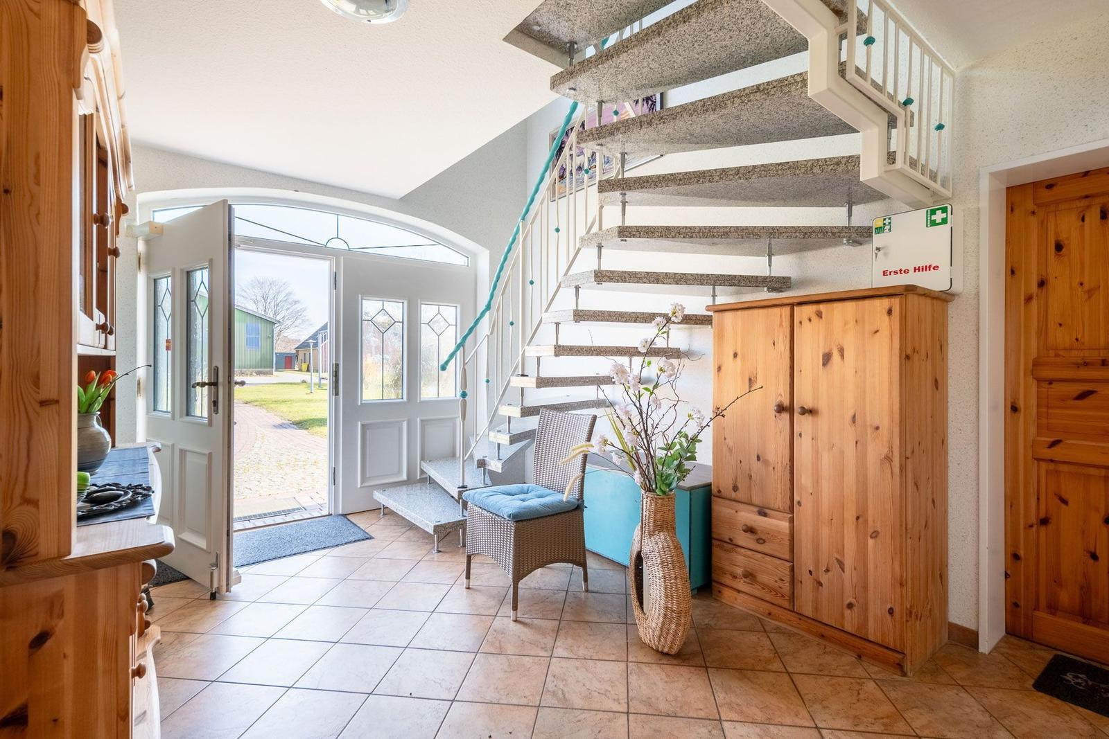 Eingangsbereich mit Treppe, Holzschränken und Glastür zur Außenterrasse.