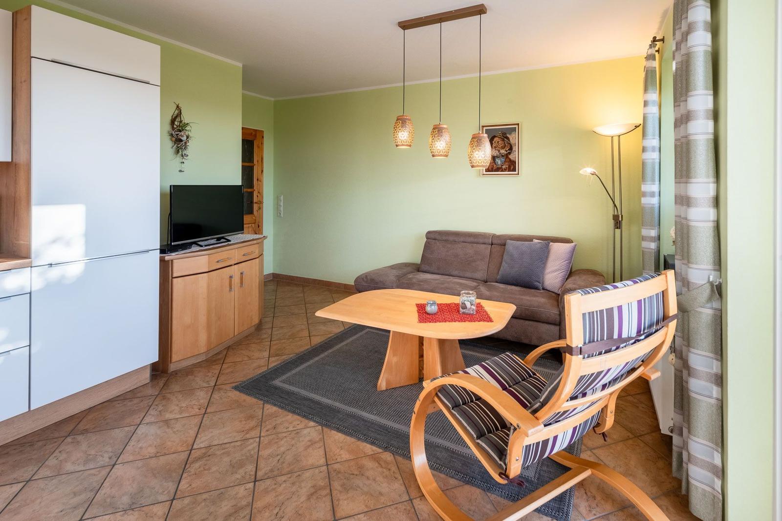 Wohnzimmer mit Sofa, Tisch und Stuhl. An der Wand hängt ein Fernseher.