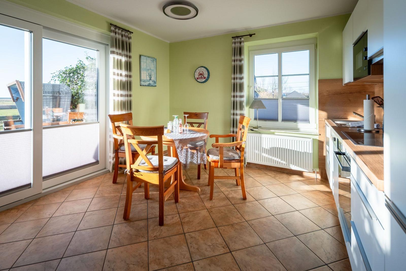 Essbereich mit Tisch, Stühlen und Küchenzeile. Durchgänge zu Terrasse und Fenster.