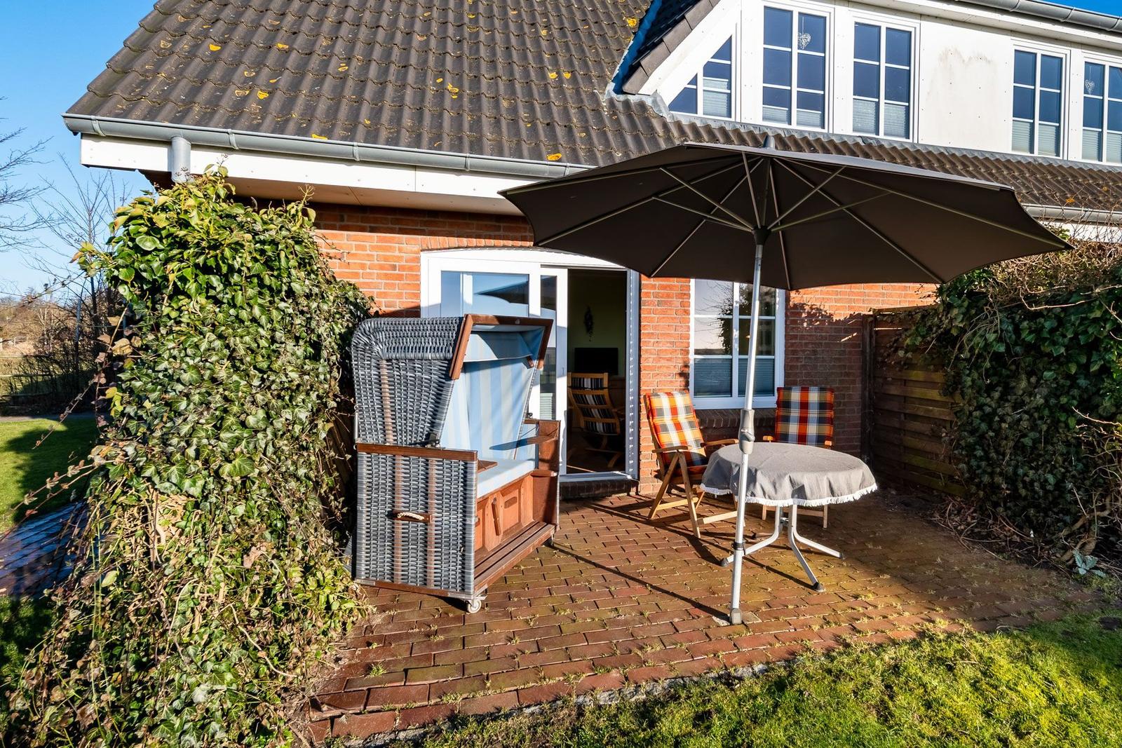Terrasse mit Sonnenschirm, Tisch, Stühlen und Strandkorb vor Haus.