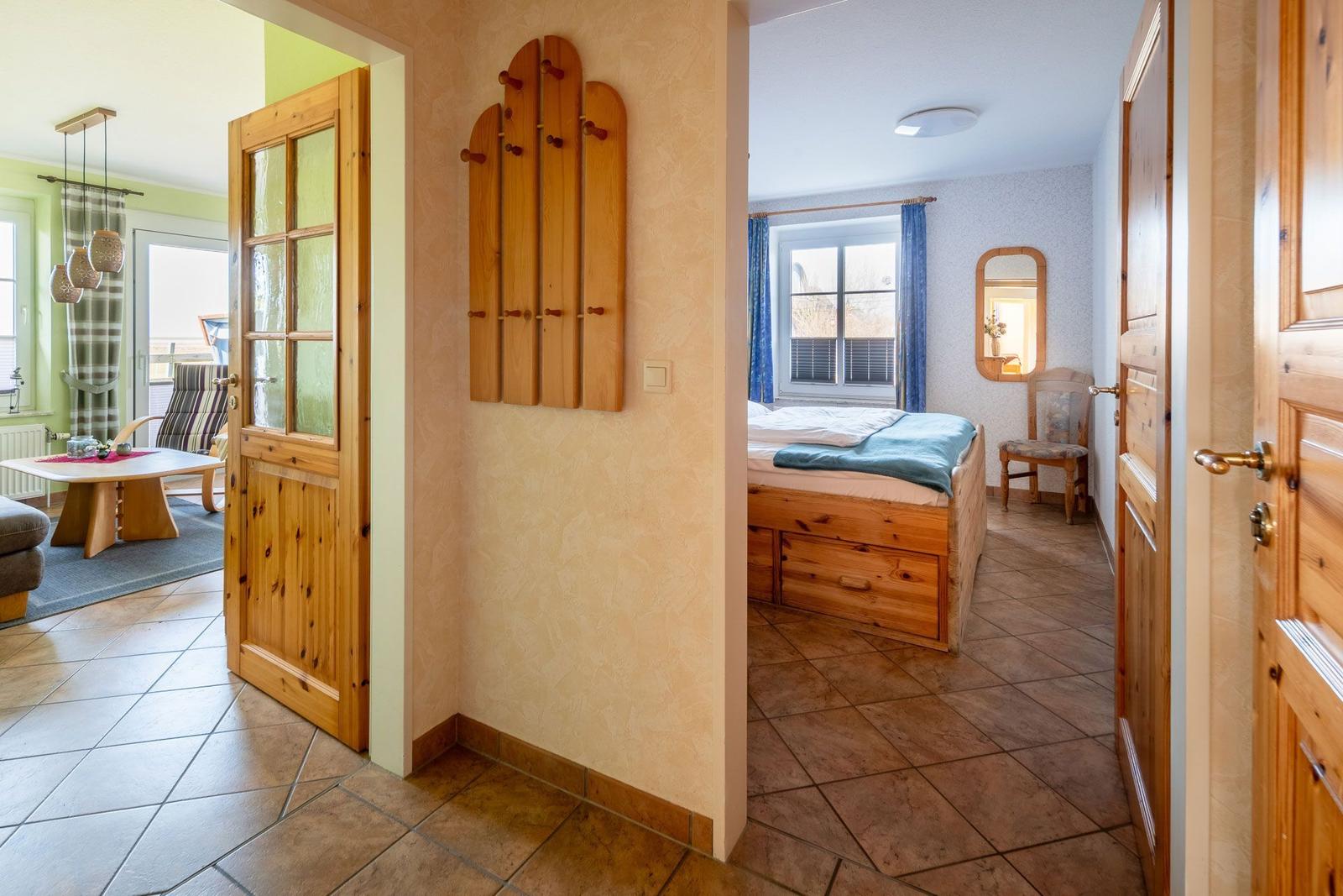 Schlafzimmer mit Holzbett und Fenster. Flur mit Holztür und Wandgarderobe. Wohnbereich mit Tisch und Stühlen.
