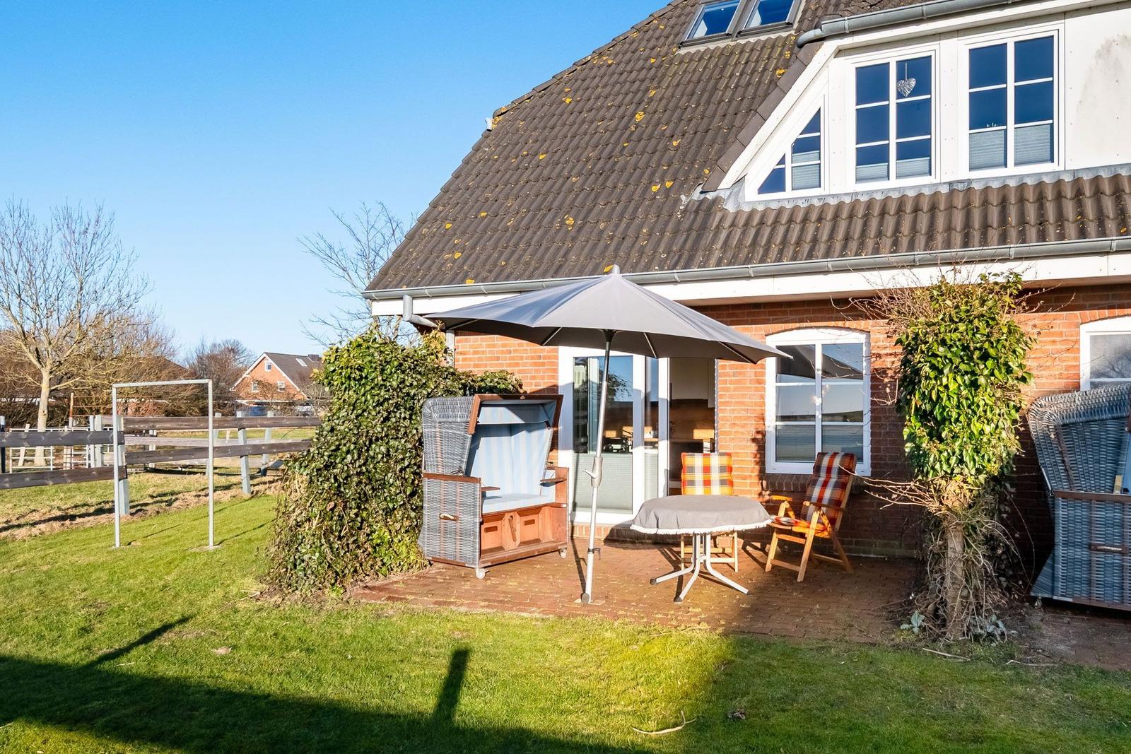 Haus mit Terrasse, Sonnenschirm, Tisch und Stühlen im Garten.