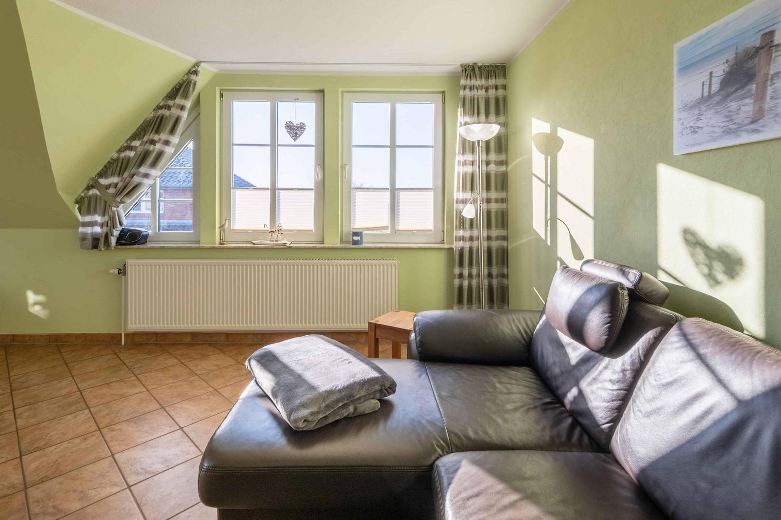 Wohnzimmer mit Sofa, Fenstern und Heizkörper.